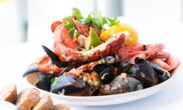A vibrant seafood platter featuring lobster, shrimp, mussels, and lemon on a white plate.